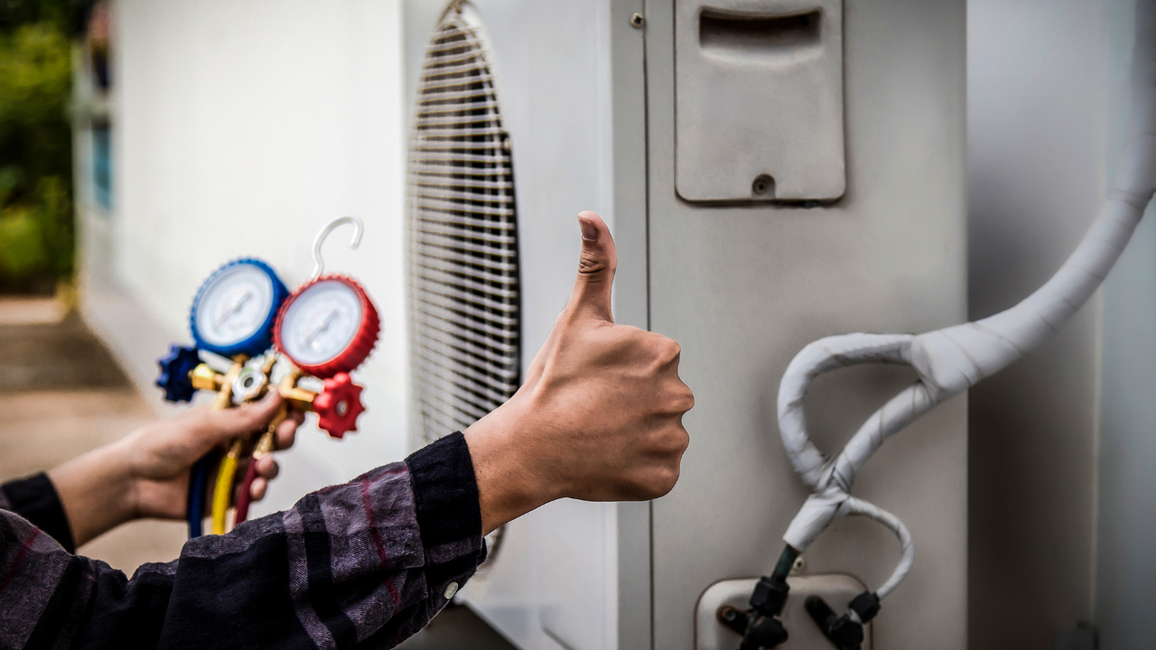 a maintenance man giving a thumbs up while he checks the refrigerant levels of an HVAC system.