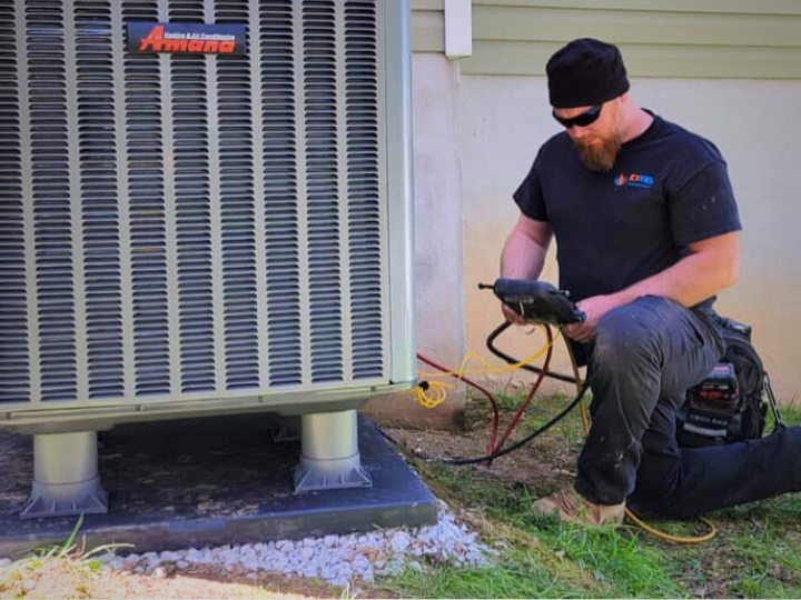 one of our technicians kneeling next to a large exterior air conditioning unit testing the refrigerant pressure