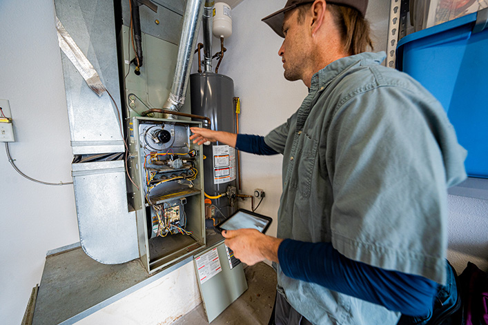 Young Male Property Inspector Photographing a Furnace Hot Water Heater and Air Conditioning Unit Inside a Residential Home Garage