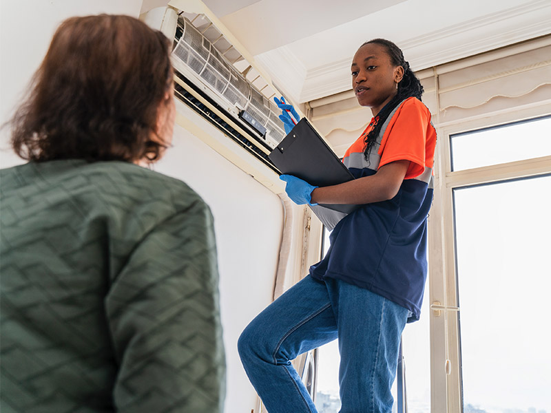 HVAC technician inspecting ductless indoor unit and discussing problems with homeowner.
