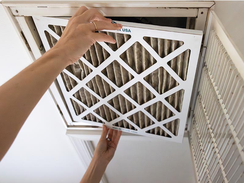 HVAC technician removing dirty air filter from intake vent.