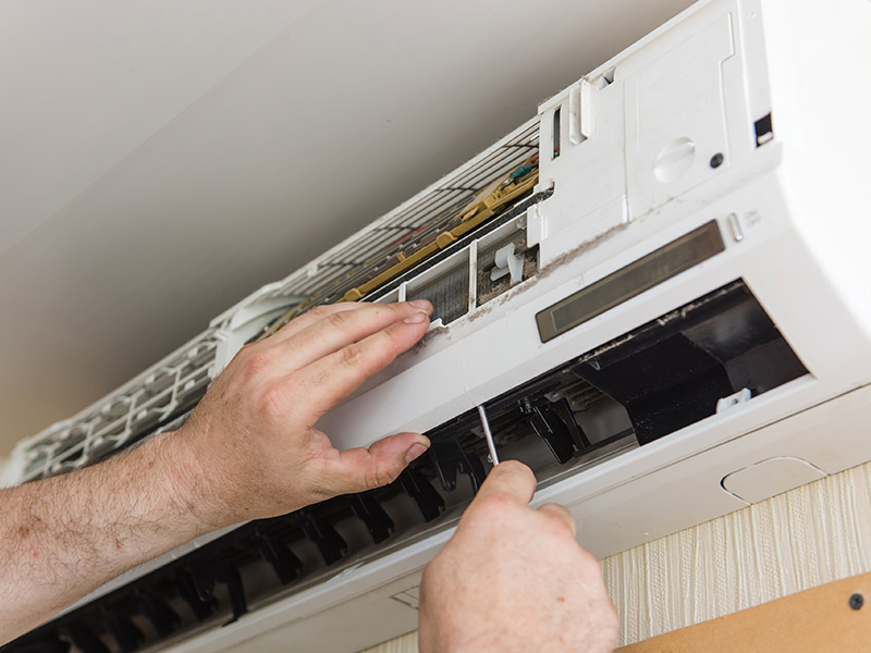 HVAC technician using screwdriver to work on indoor AC wall unit.