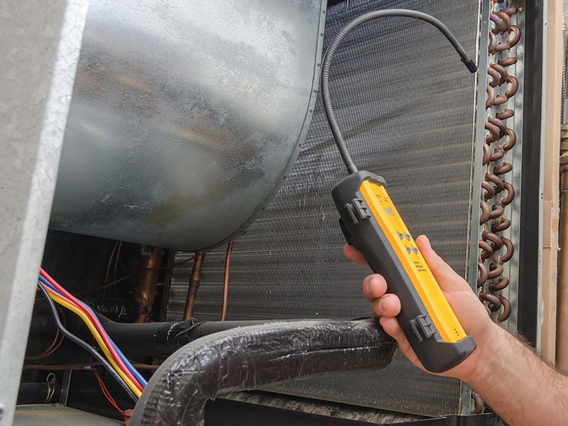 Technician using tool to check for HVAC refrigerant leak.