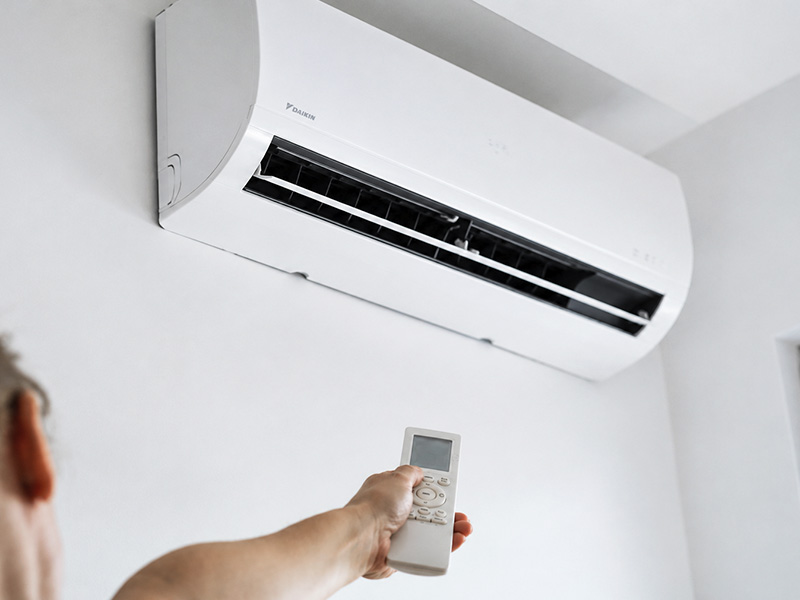 Woman pointing remote at wall-mounted mini-split unit.