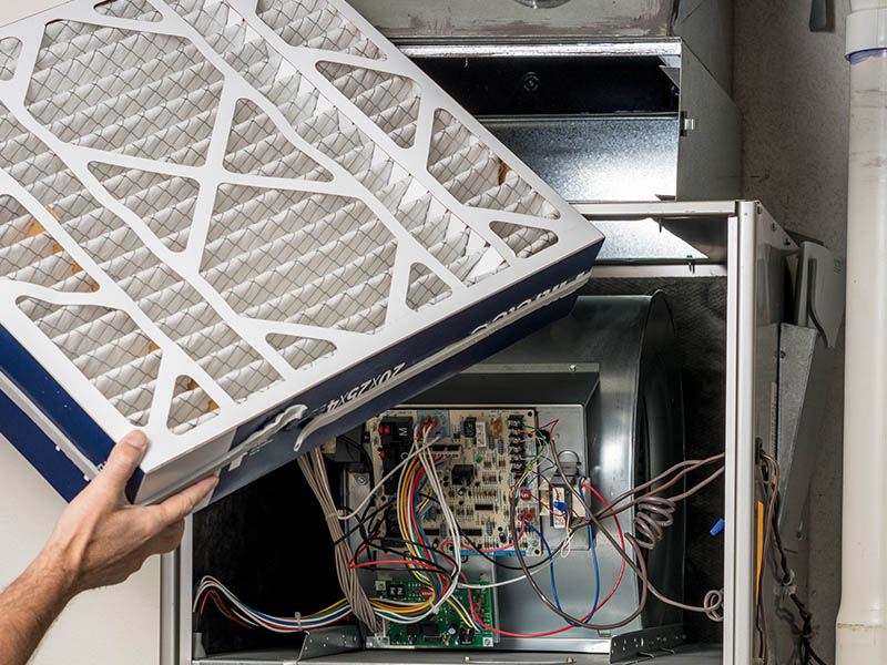 Male HVAC technician placing a new filter into a home furnace.